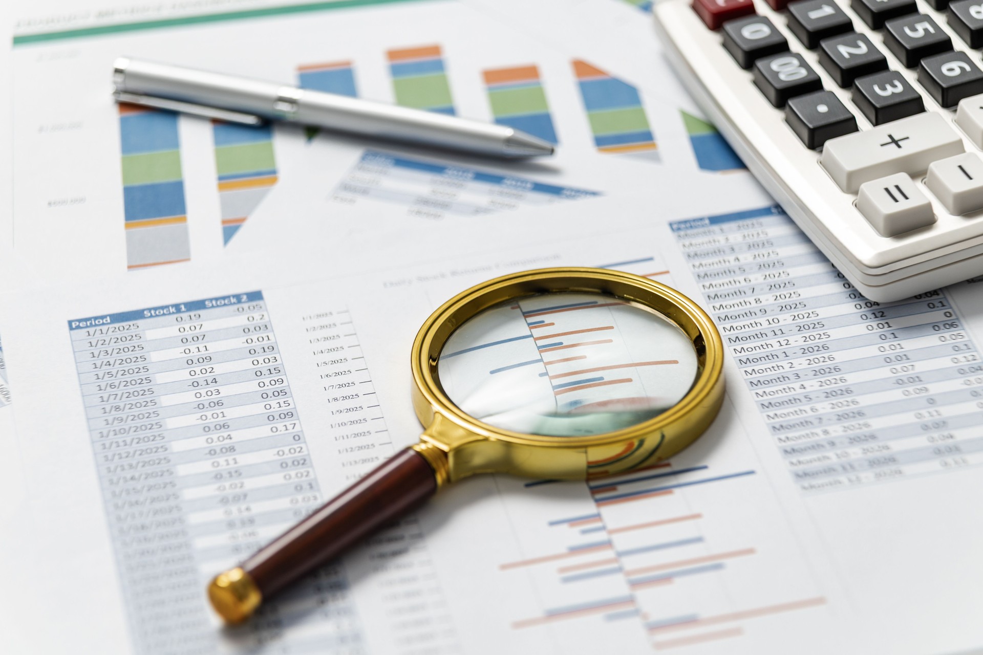 Analyzing financial reports with a magnifying glass, calculator, and pen on a desk
